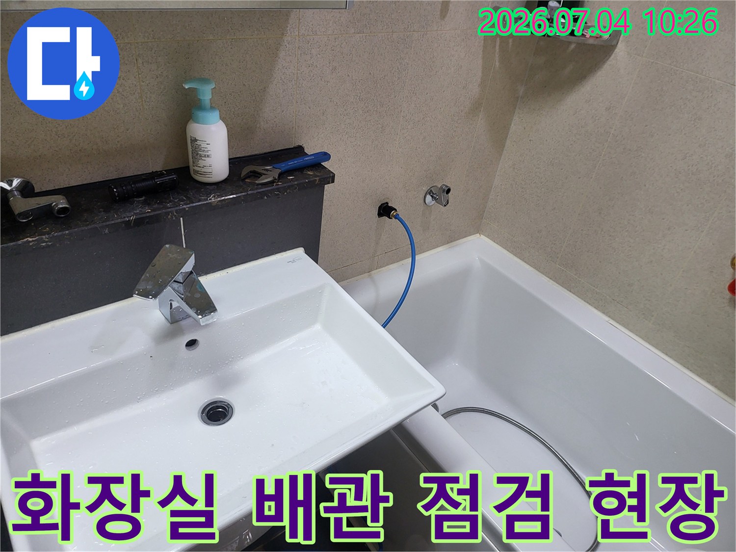 세면대 옆쪽 노출된 파란색 배관과 샤워기 호스가 연결된 화장실 내부 모습