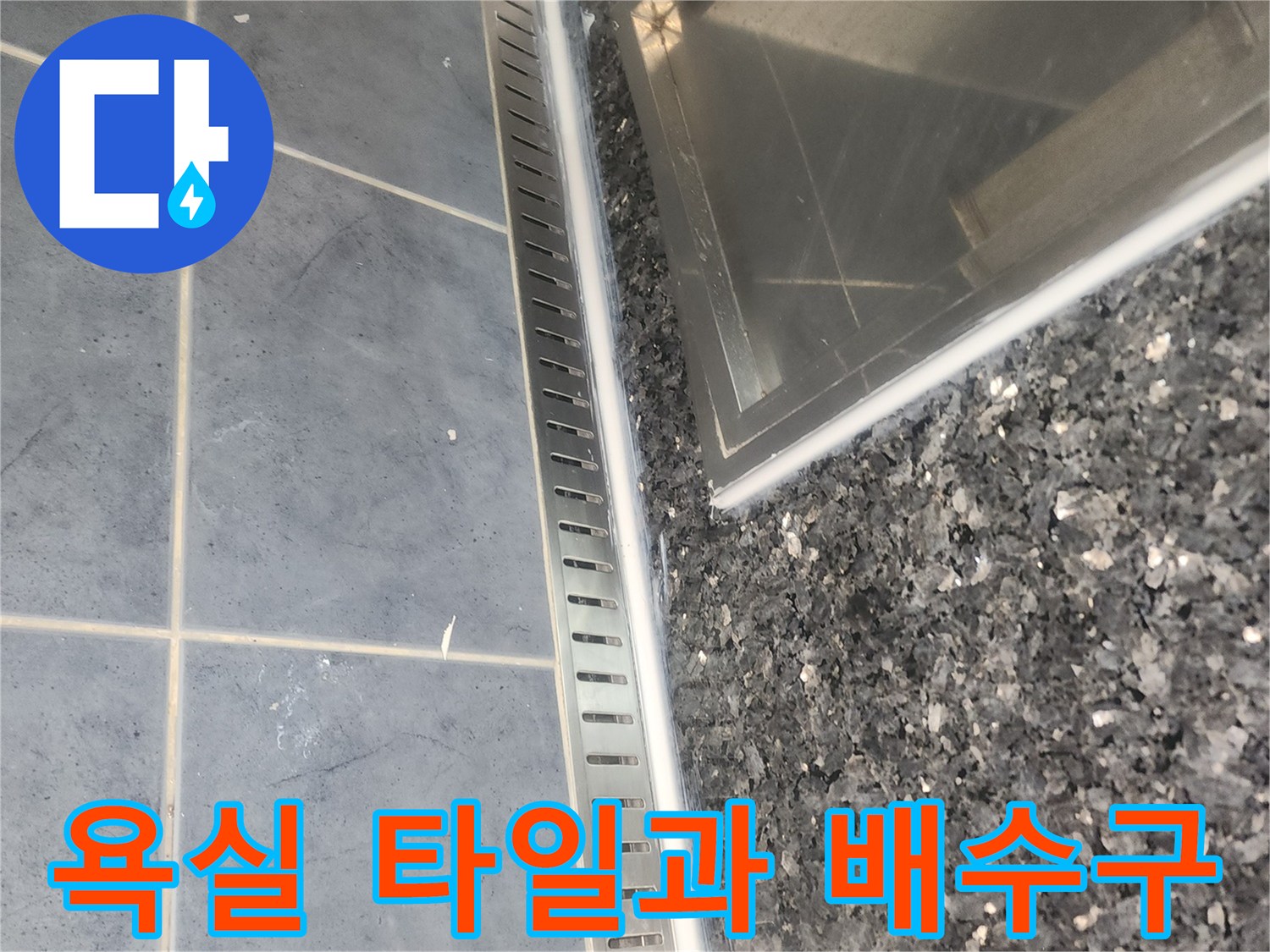 어두운색의 욕실 타일과 스테인리스 배수 덮개 모습