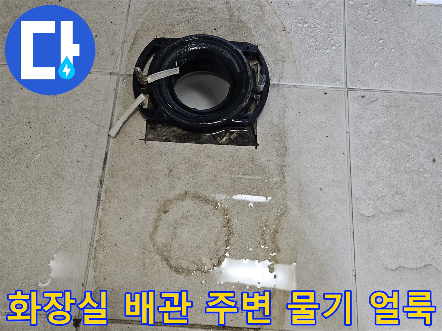화장실 타일 바닥의 배관 연결 부위 주변에 넓게 퍼진 젖은 얼룩과 노출된 배관 상태