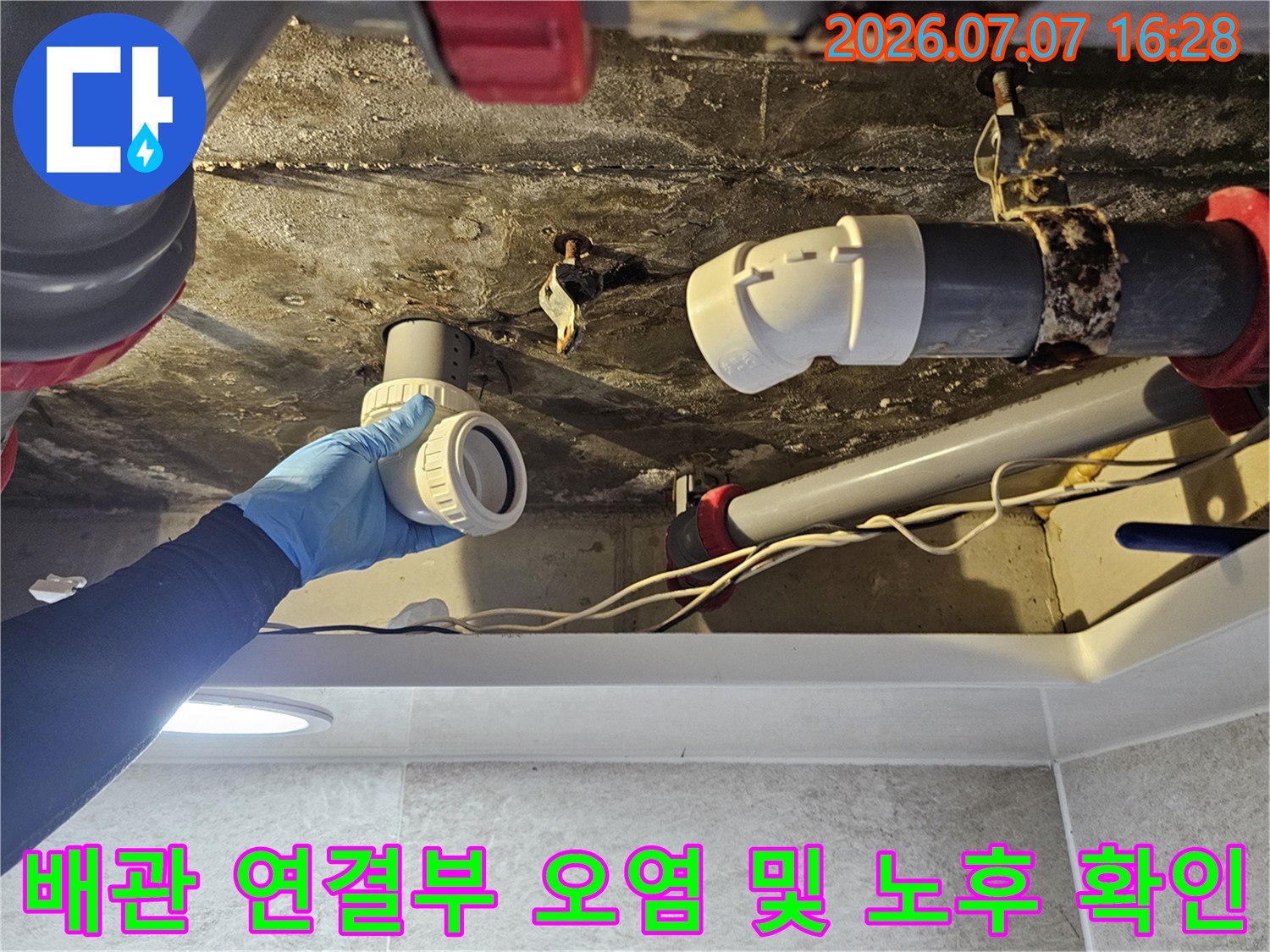 노후되어 변색된 배관 부품과 새 교체용 자재를 대조하며 점검하는 장면