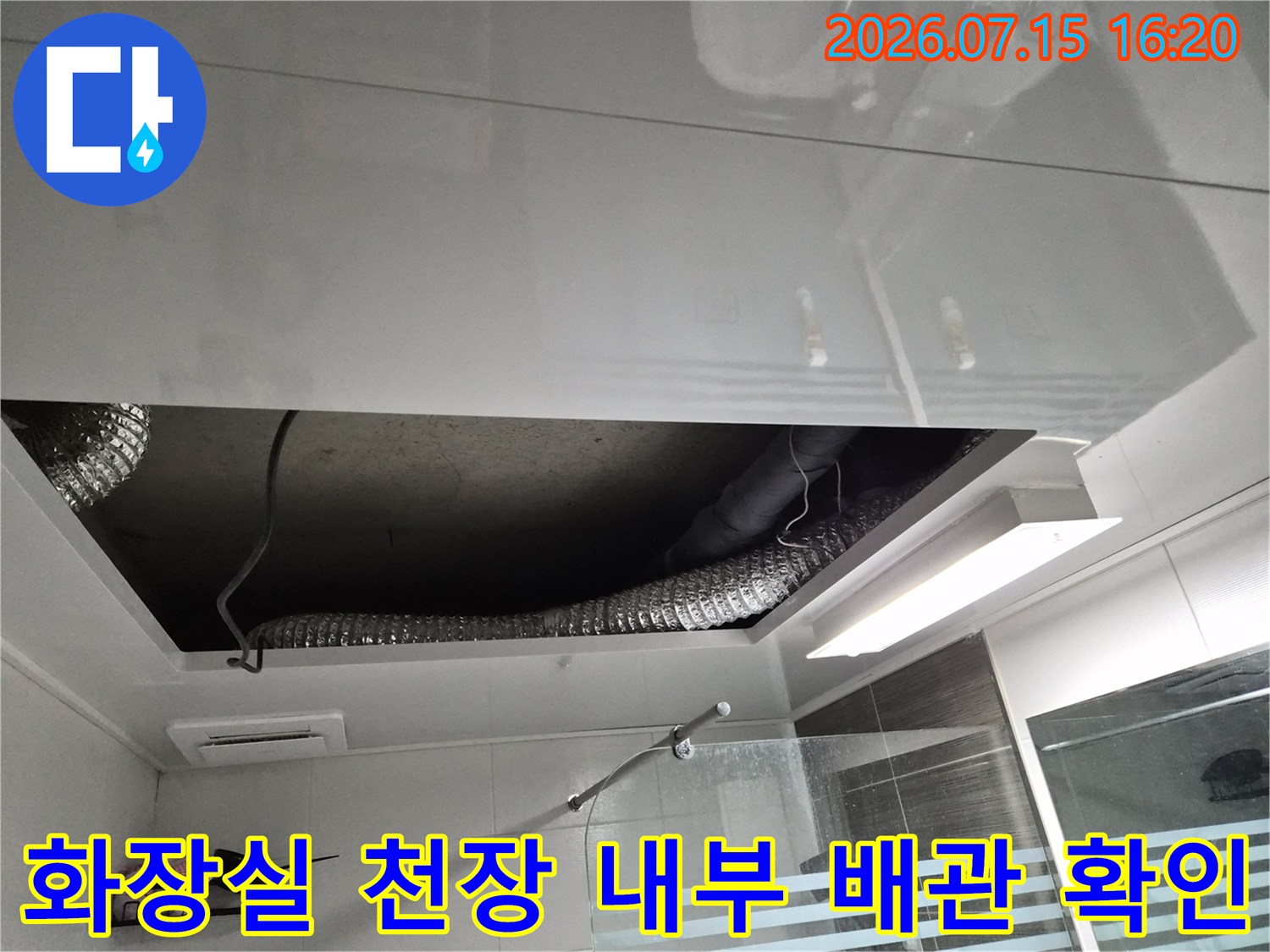 화장실 천장재를 제거하고 노출된 은색 자재와 상부 배관 구조를 점검하는 모습