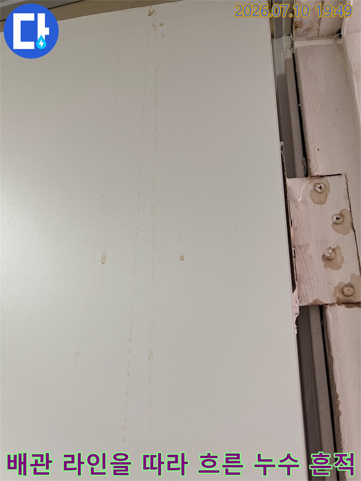 흰색 천장 마감재 위에 끈적하게 남은 갈색 누수 얼룩과 배관라인