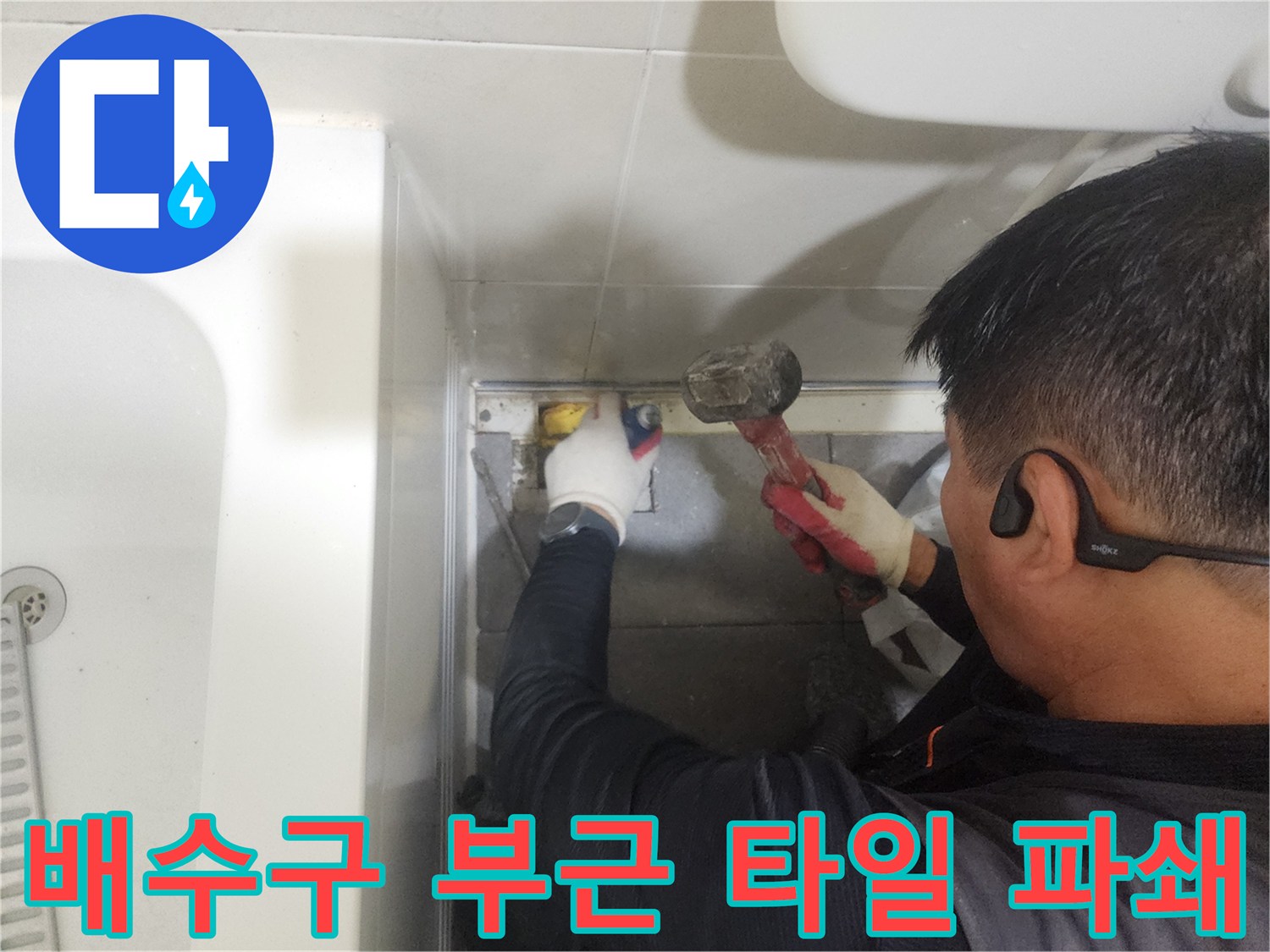 엔지니어가 망치를 사용하여 욕실 배수구 주변의 낡은 마감재를 제거함