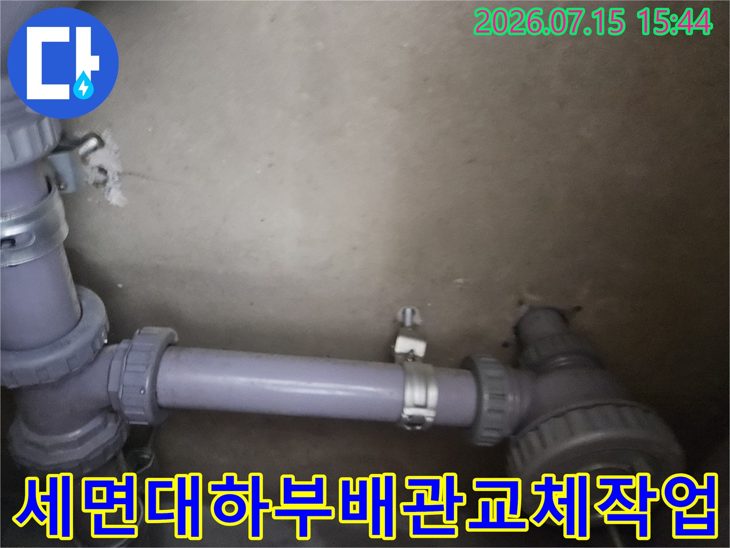 세면대 하단에 위치한 보라색 배관과 연결 부속의 교체 작업 현장