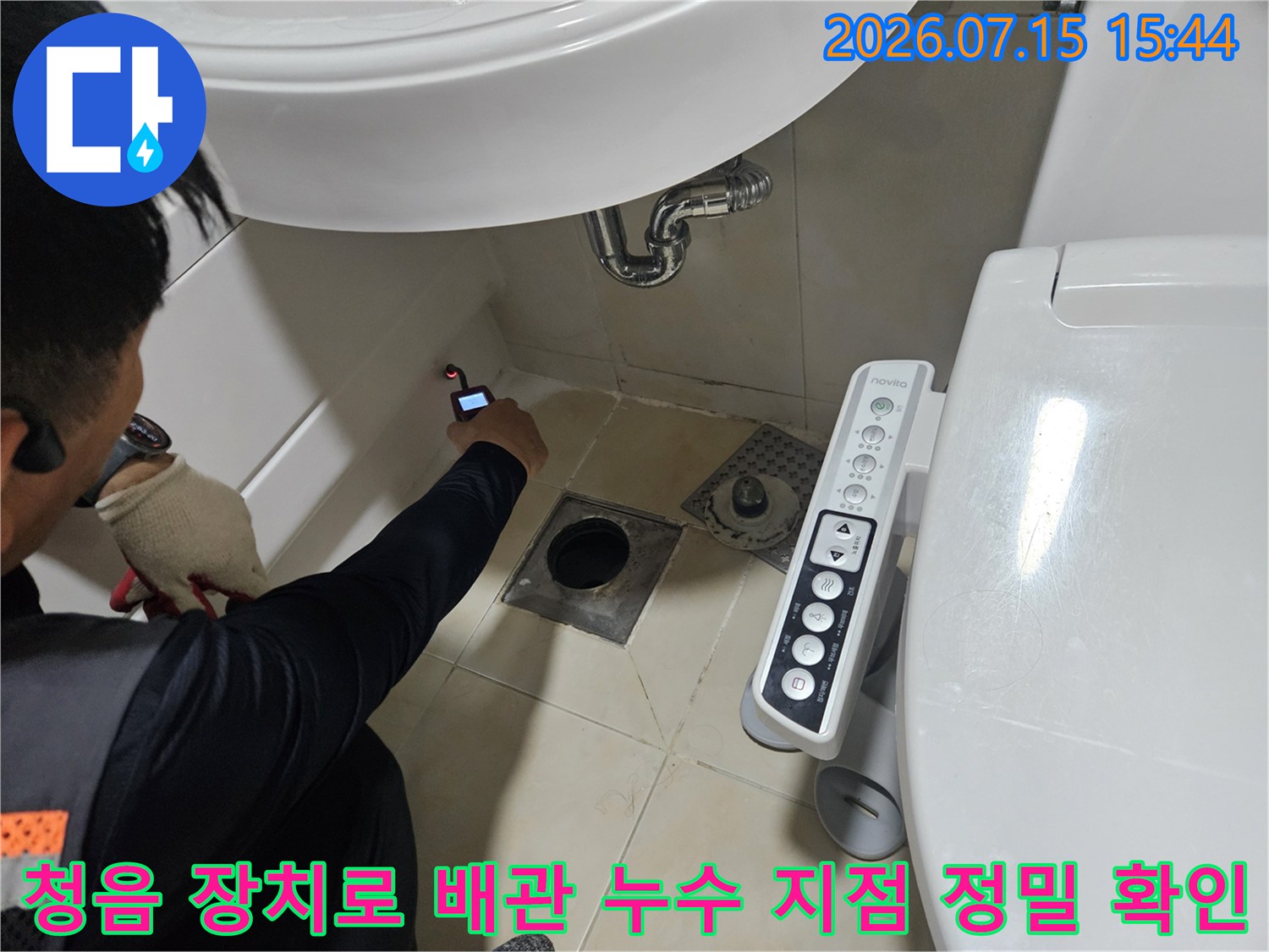 세면대 하부 공간에서 청음 탐지기를 사용하여 배관의 이상 유무를 세밀하게 진단하는 모습