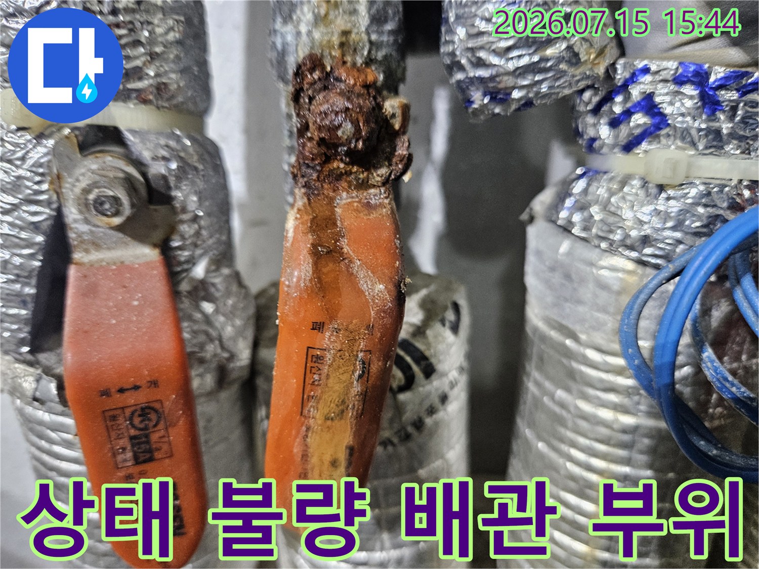 오렌지색 배관과 노후된 관재가 엉켜 있는 누수 의심 지점의 근접 촬영