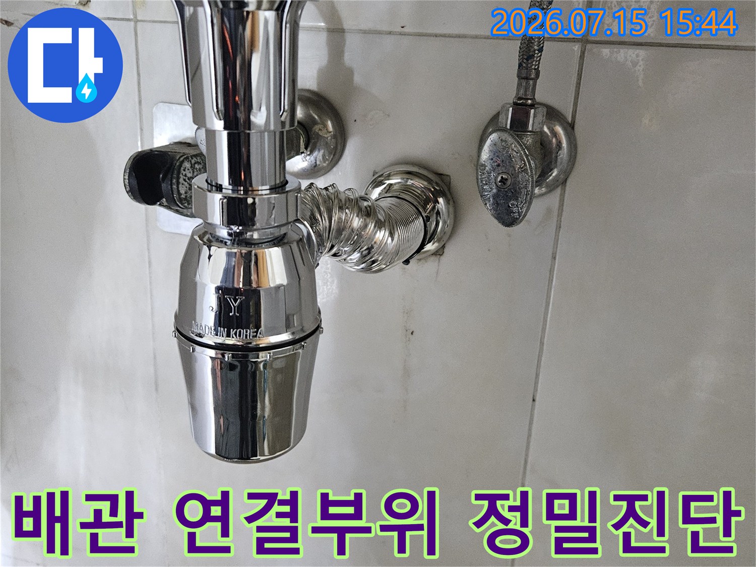 욕실 내 세면대 아래 위치한 금속 배관과 연결 구조를 촬영한 사진
