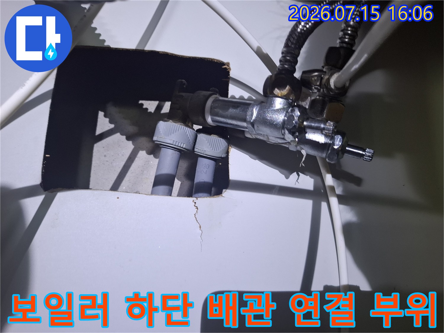 보일러 아래쪽의 금속 밸브와 회색 플라스틱 배관이 연결된 모습