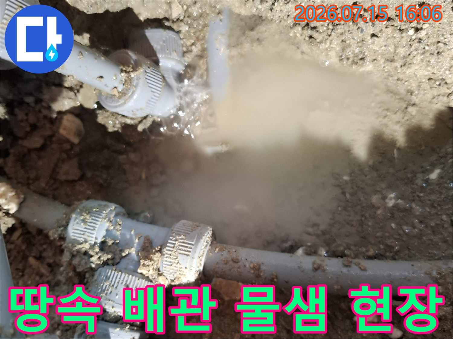 흙 속에 매립된 회색 플라스틱 배관 연결 부위에서 물이 뿜어져 나오는 모습