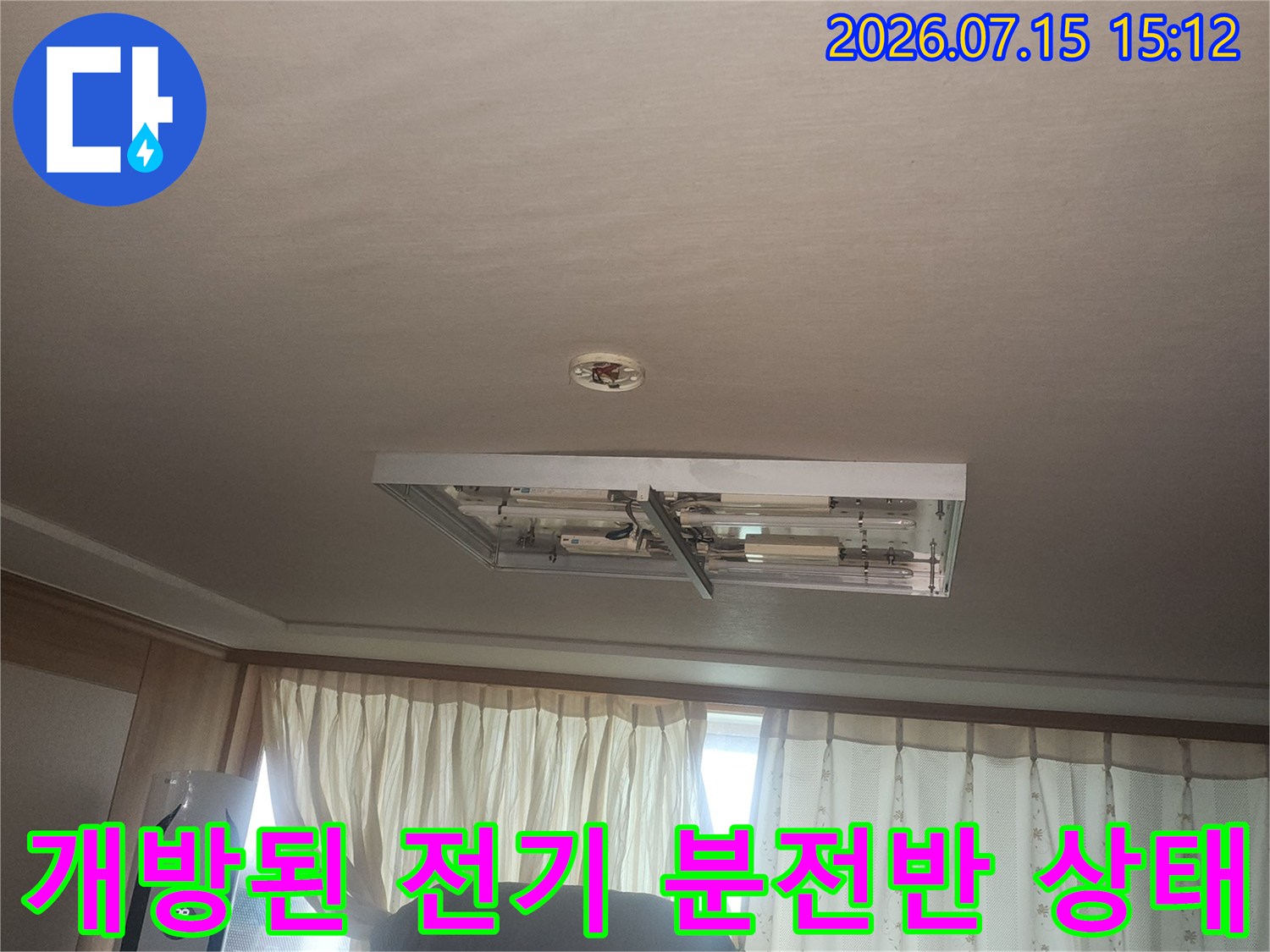 벽면에 설치된 흰색 배전함의 커버가 열려 내부 전선들이 노출된 장면