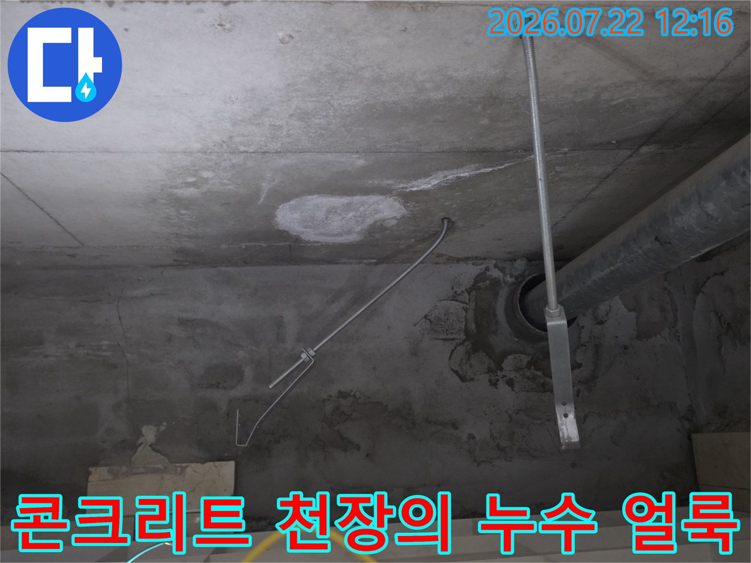 회색 콘크리트 천장에 배관과 지지대가 설치되어 있고 주변에 누수 흔적이 보이는 사진