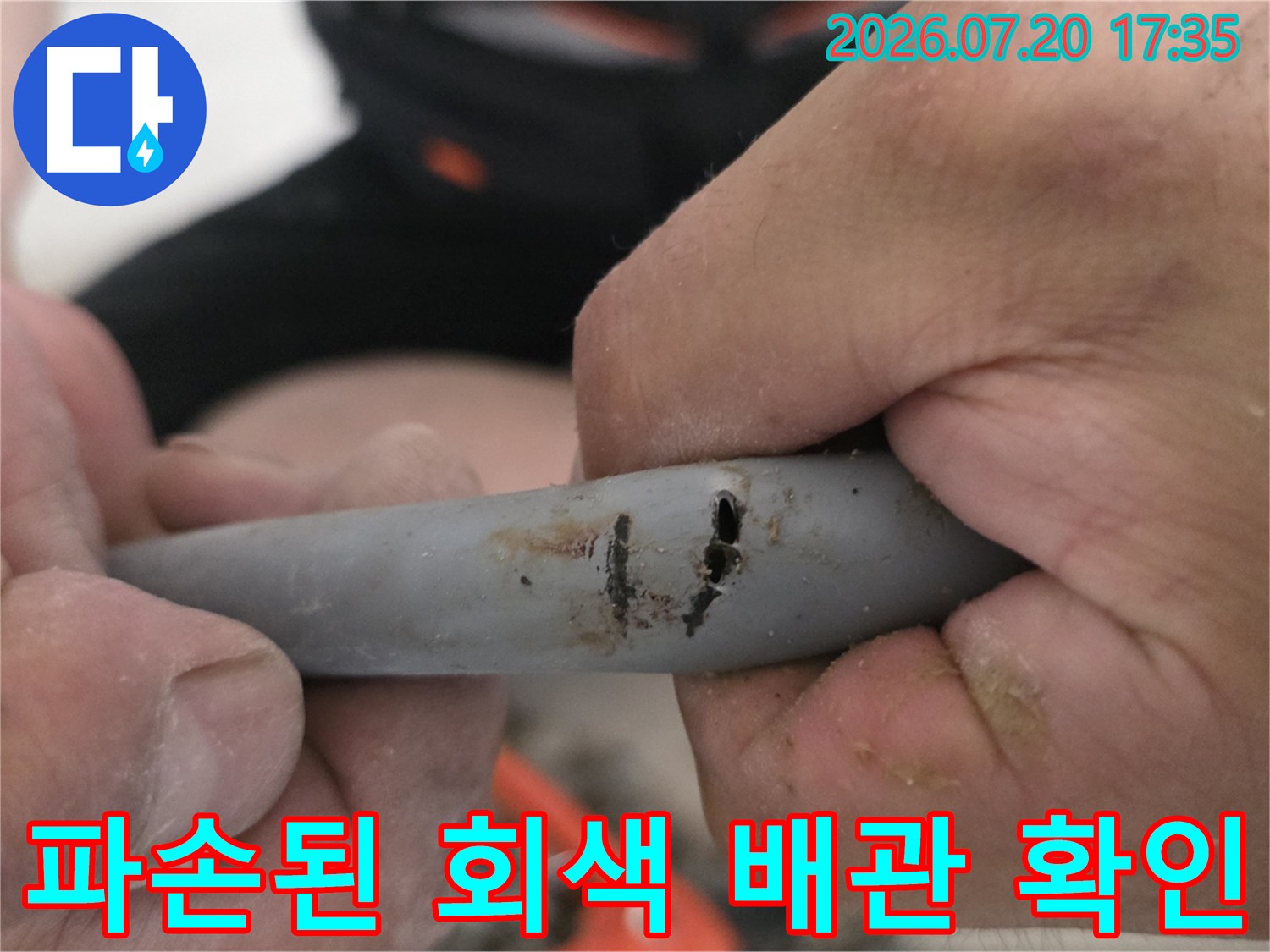 손으로 파손 부위를 잡고 있는 회색 배관의 모습