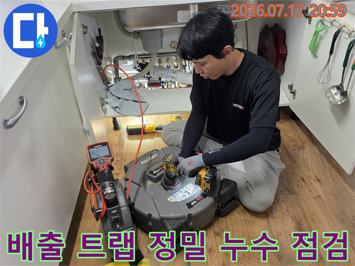 전문 기술자가 싱크대 아래 배출 트럼과 연결부의 누수 가능성을 탐지기로 확인하는 모습