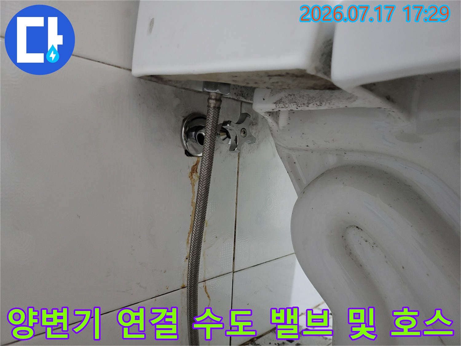흰색 욕실 타일을 배경으로 설치된 변기용 급수 밸브와 금속제 유연 호스의 근접 사진