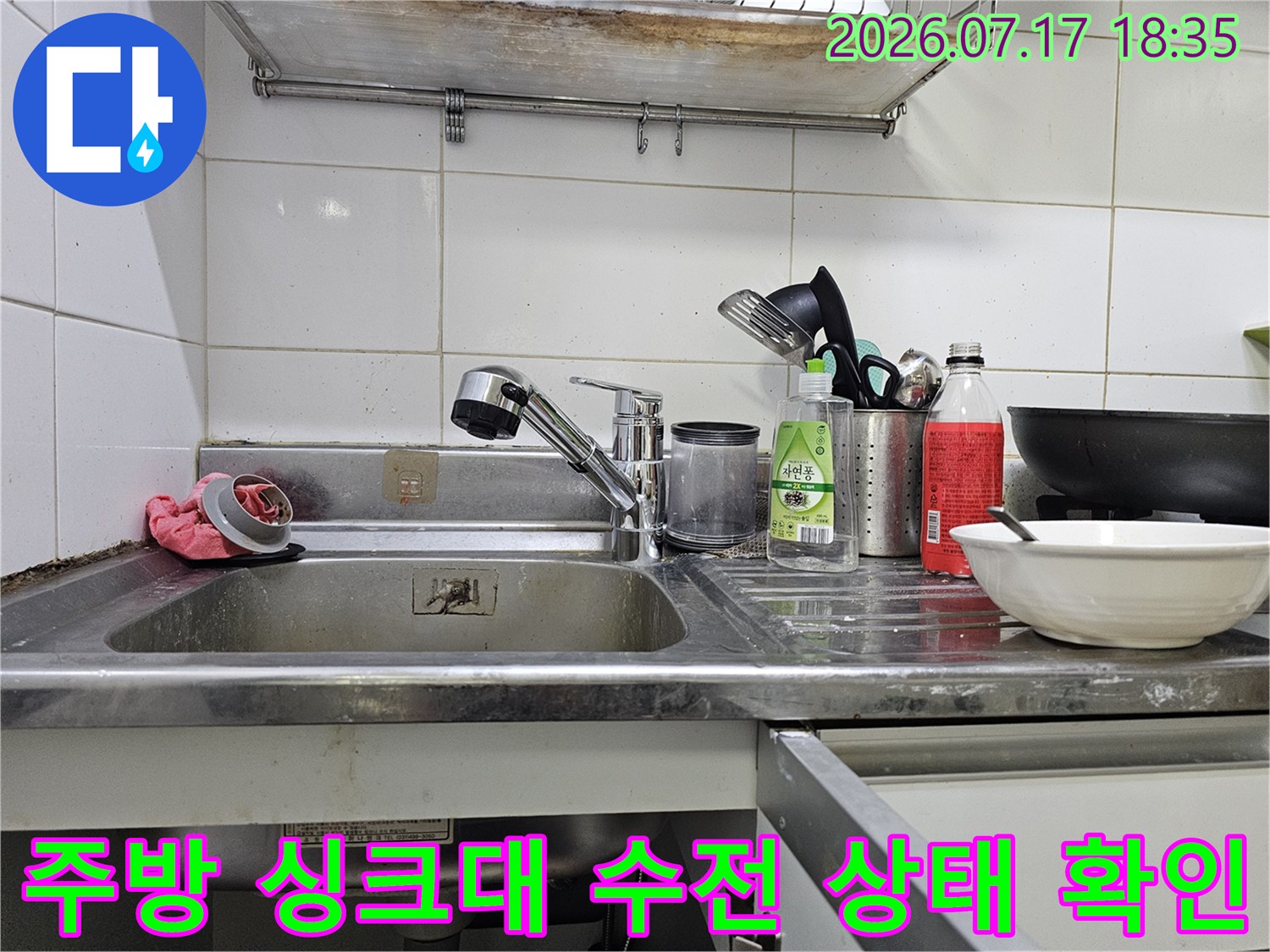 흰색 타일 벽면 앞에 설치된 스테인리스 소재의 주방 싱크대와 수전-세척도구들