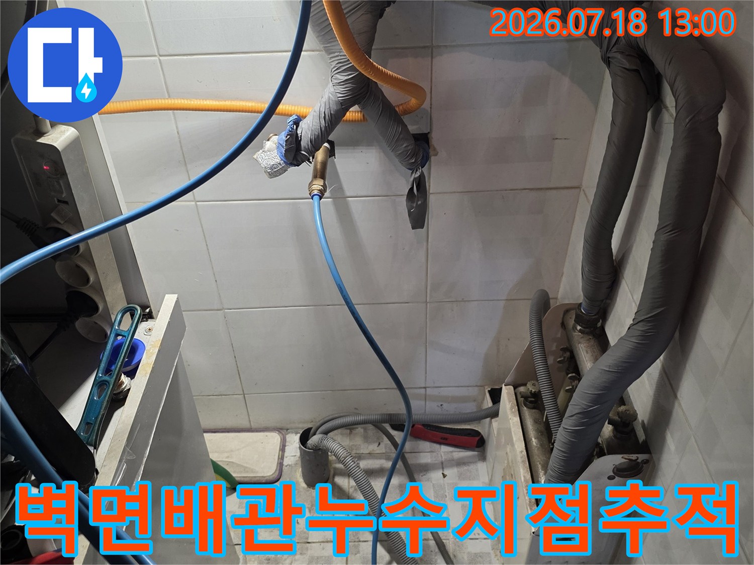 회색 보온재가 감싸진 벽면 배관에 파란색과 노란색 호스가 연결되어 측정 중인 사진