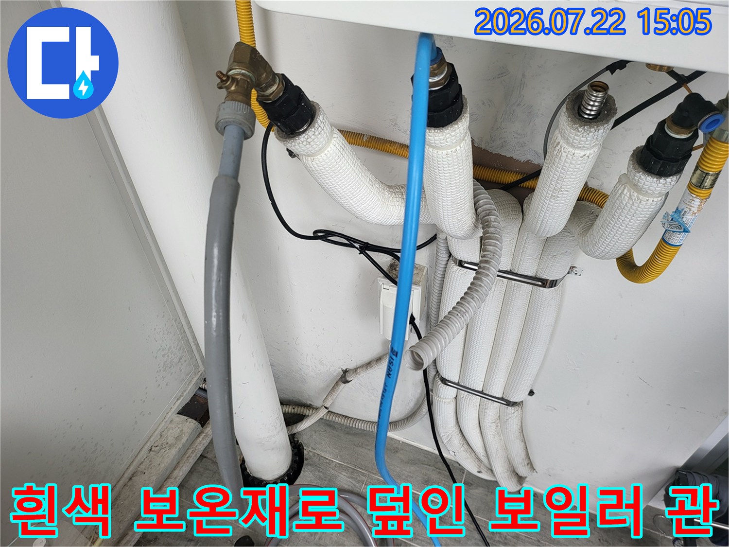 보일러 아래쪽에 설치된 흰색 보온재 배관들과 파란색 플라스틱 호스-배관 고정 장치 모습