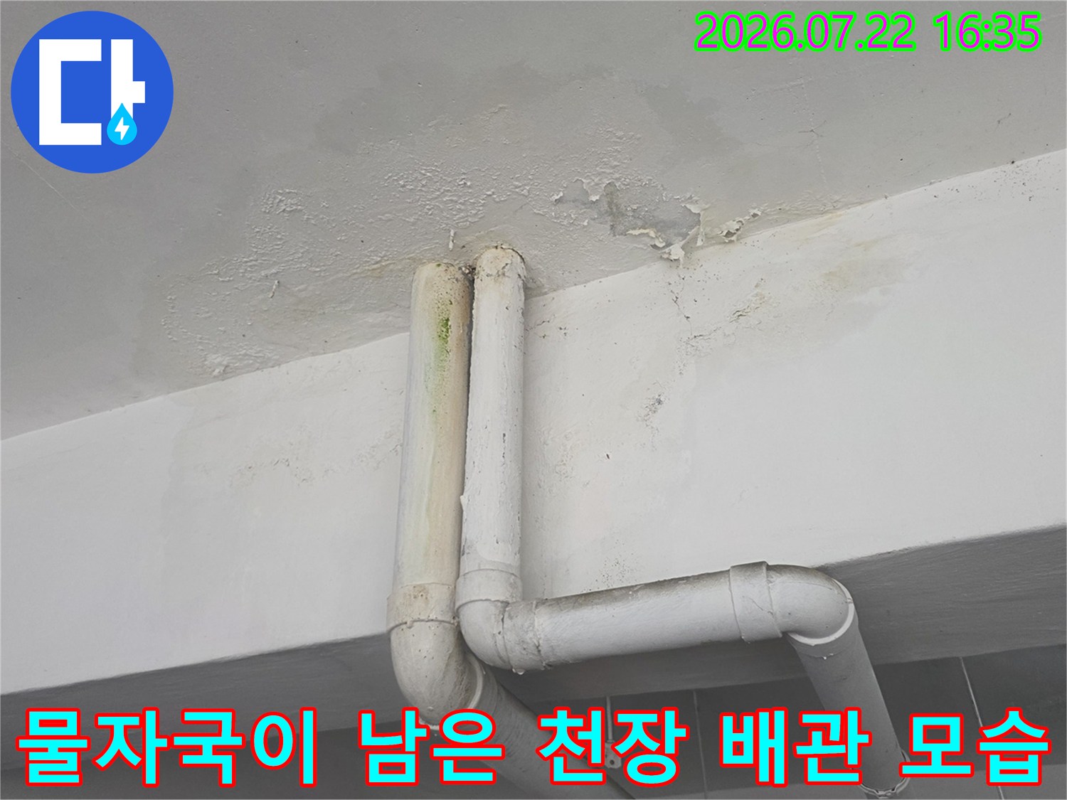 천장 마감재 사이로 흰색 플라스틱 배관이 지나가며 주변에 누수 얼룩이 형성된 사진
