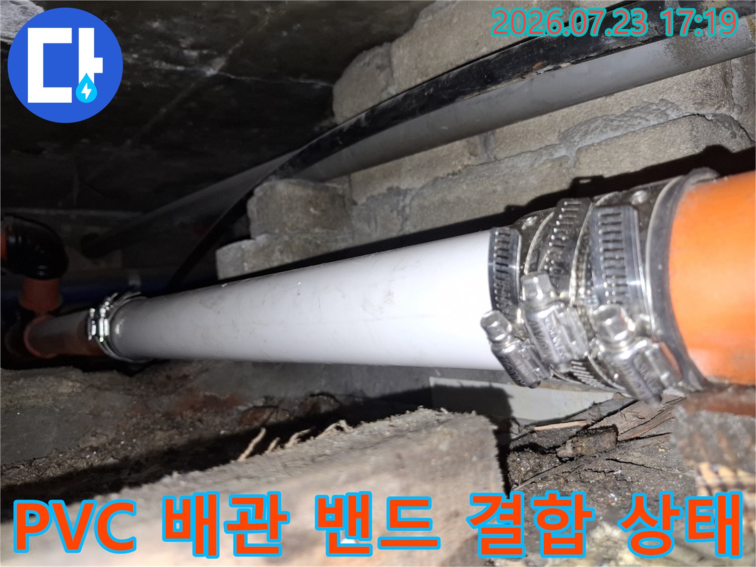 금속제 호스 밴드가 흰색과 주황색 배관 연결부를 강하게 조이고 있는 사진