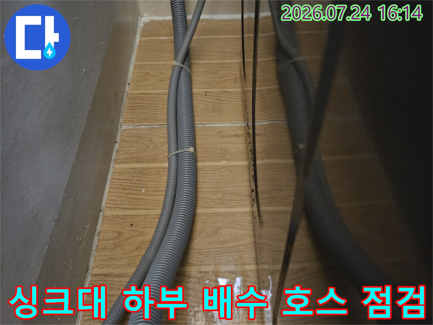 싱크대 아래 복잡하게 얽힌 회색 배수관과 타일 벽면의 연결 부위 모습