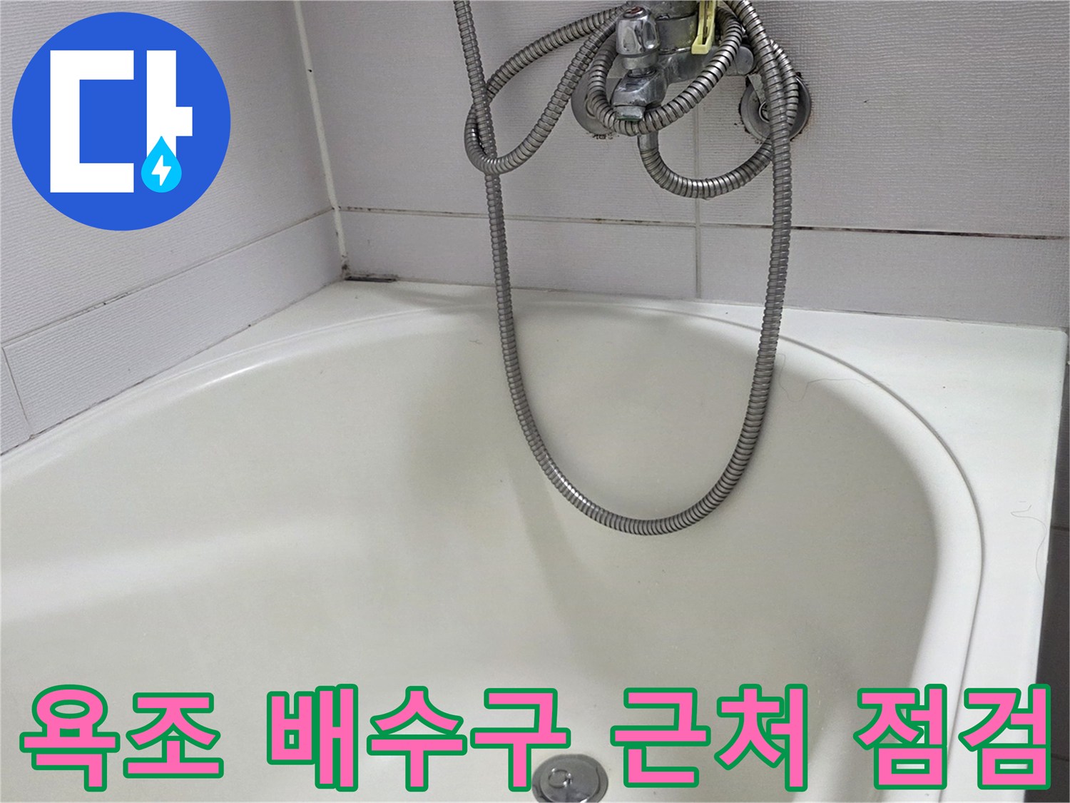욕조 바닥의 은색 배수구와 샤워기 호스 모습입니다.