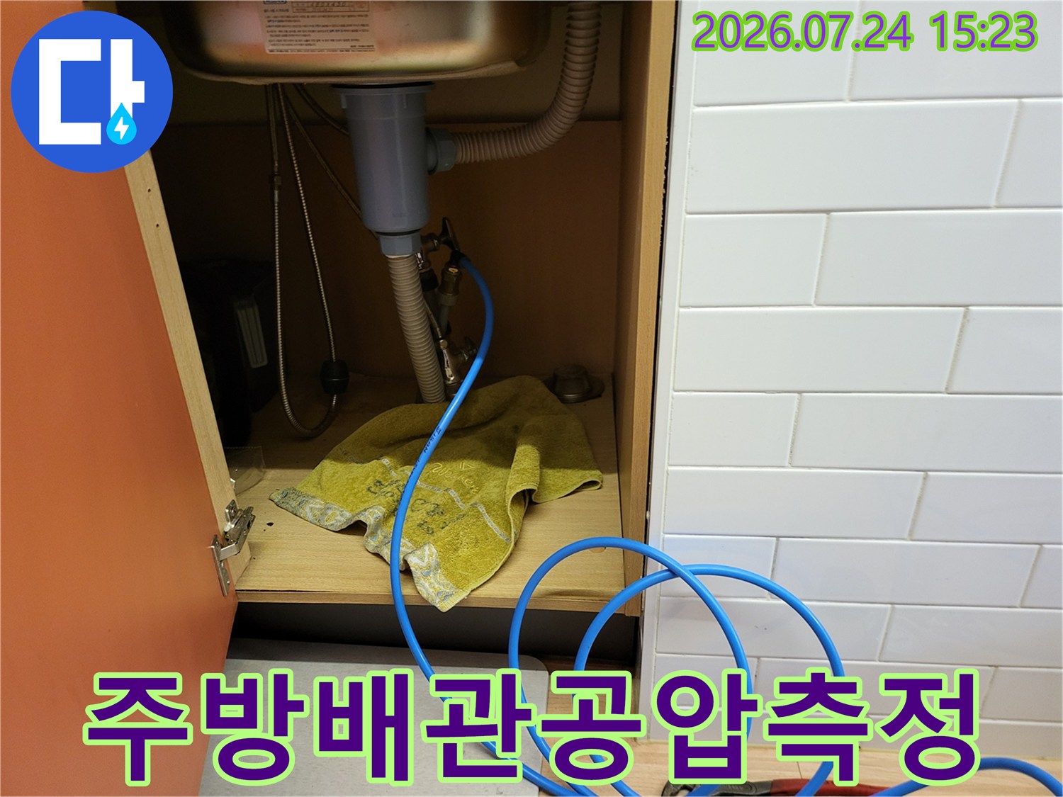 싱크대 하단 배관 연결 부위에 파란색 압력 측정용 호스가 연결된 장면