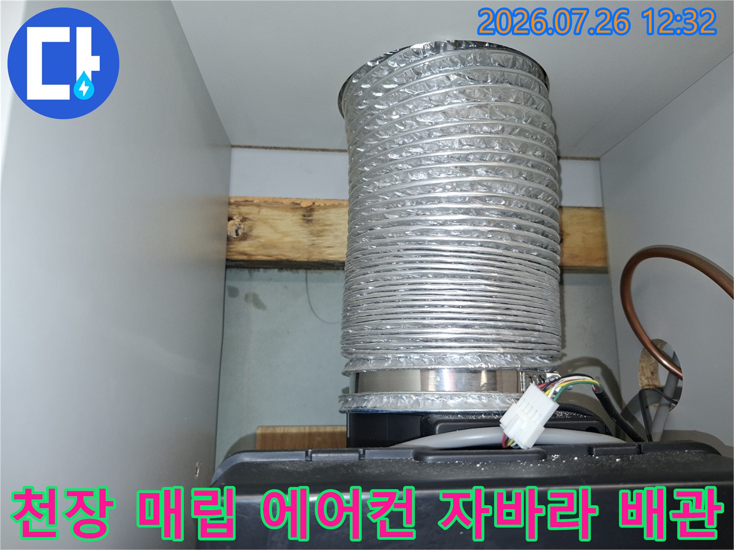 흰색 천장 구조물 사이로 설치된 은색의 주름진 에어컨 응축수 배출용 호스-배관 하단 연결부