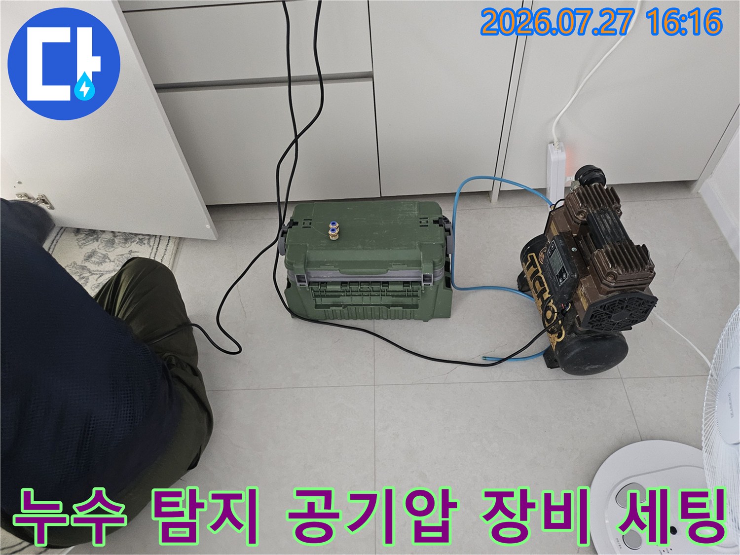 누수 지점을 찾기 위해 바닥에 배치된 녹색 압력 콤프레샤와 측정 장비-파란색 호스로 연결된 모습