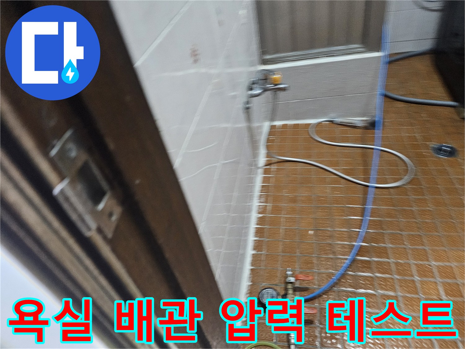 욕실 바닥 타일 위로 설치된 공압 테스트 장비와 파란색 호스 모습