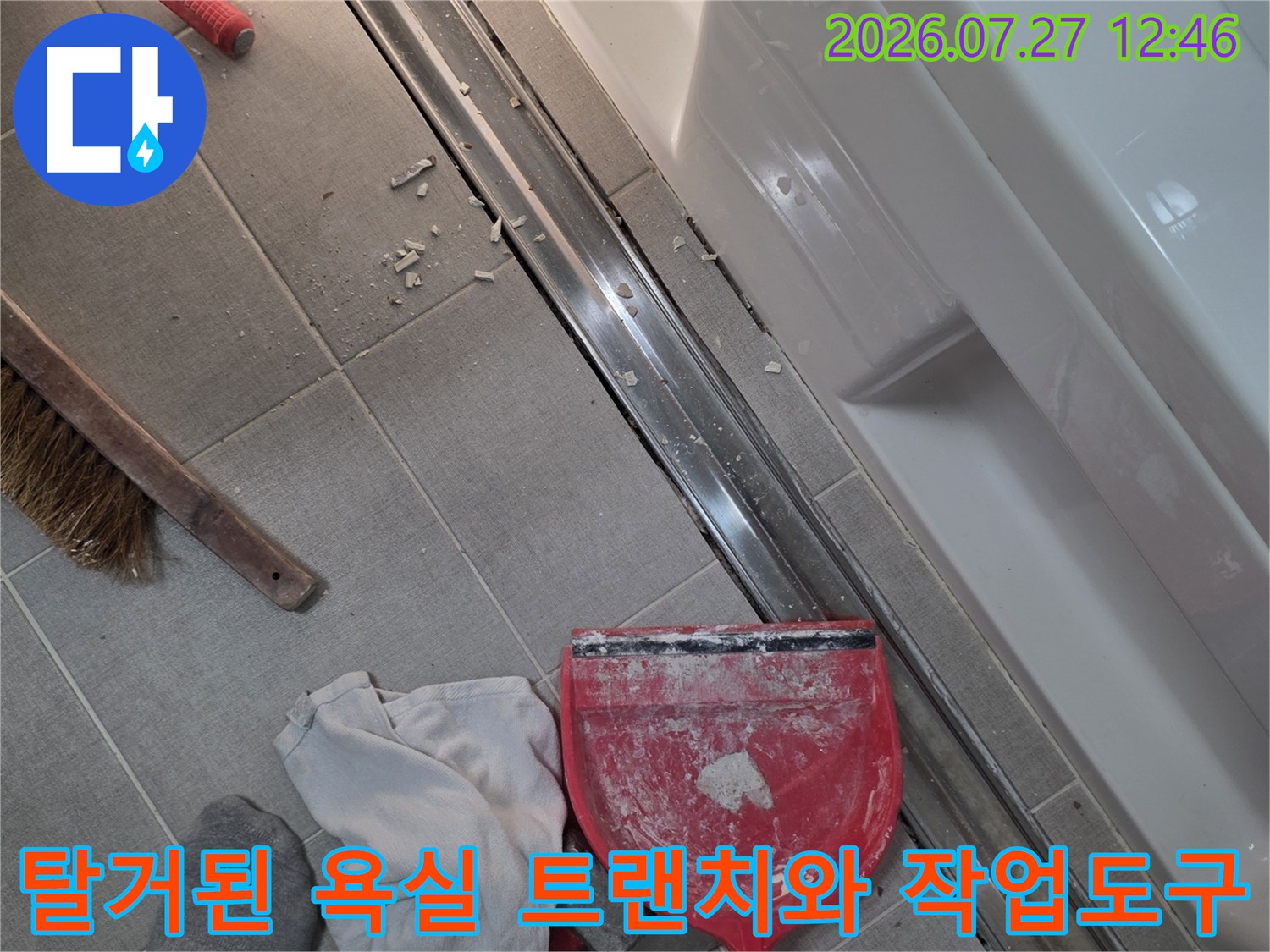 욕실 바닥의 금속제 트랜치가 탈거되어 있고 주변에 빨간색 쓰레받기와 청소 도구가 놓여 있는 모습