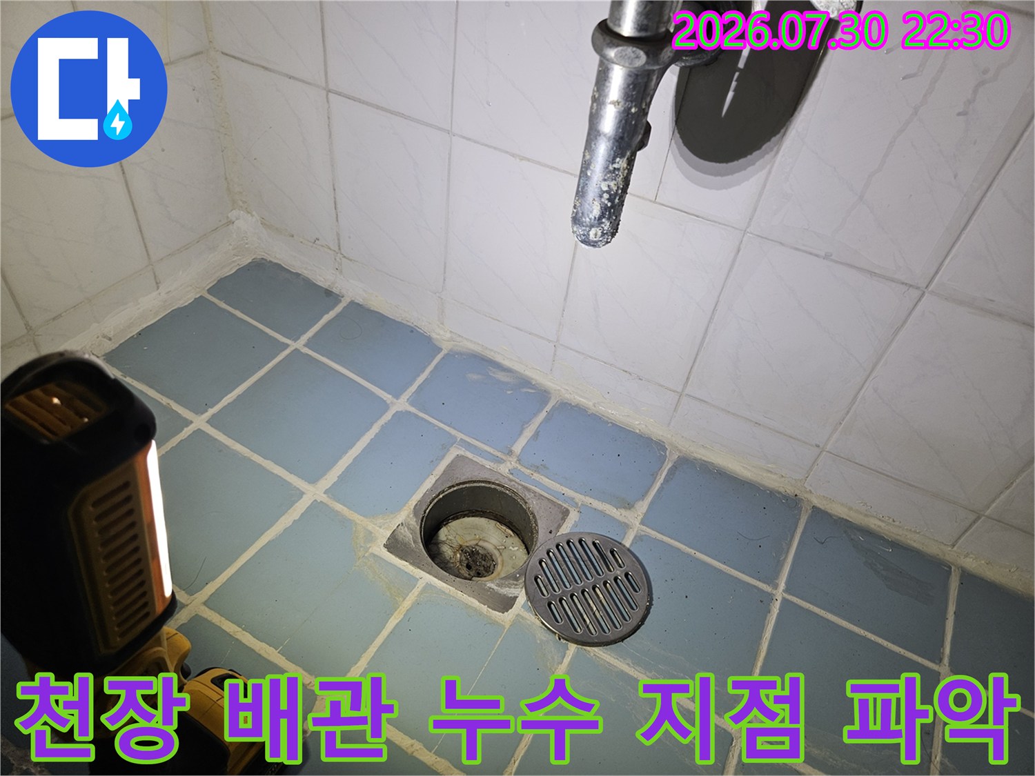 파란색 타일 천장의 배수구와 하수배관 연결부를 정밀 점검하는 장면