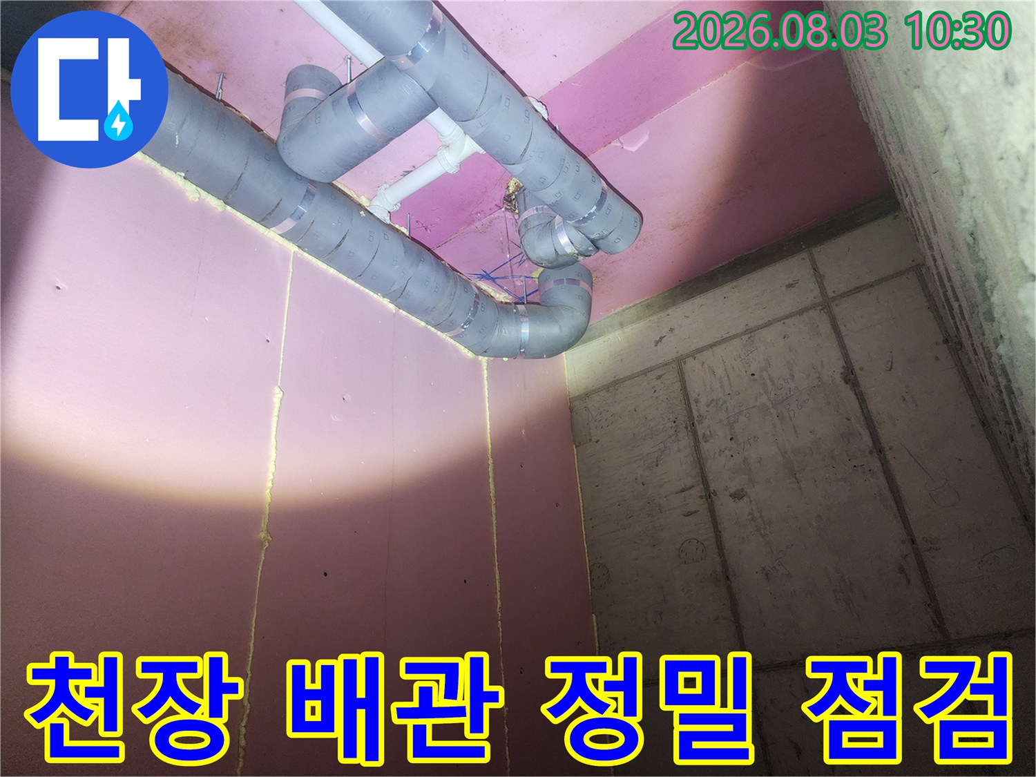 분홍색 천장 아래 노출된 회색 배관과 굴곡진 연결 부위 모습