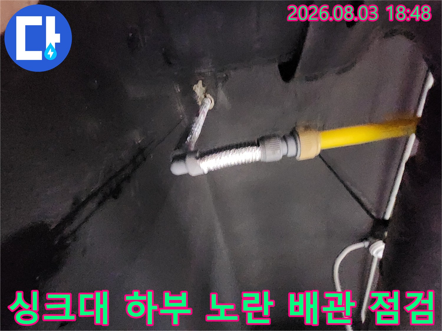 노란색 배관과 유연한 호스가 연결된 싱크대 하부 공간의 모습