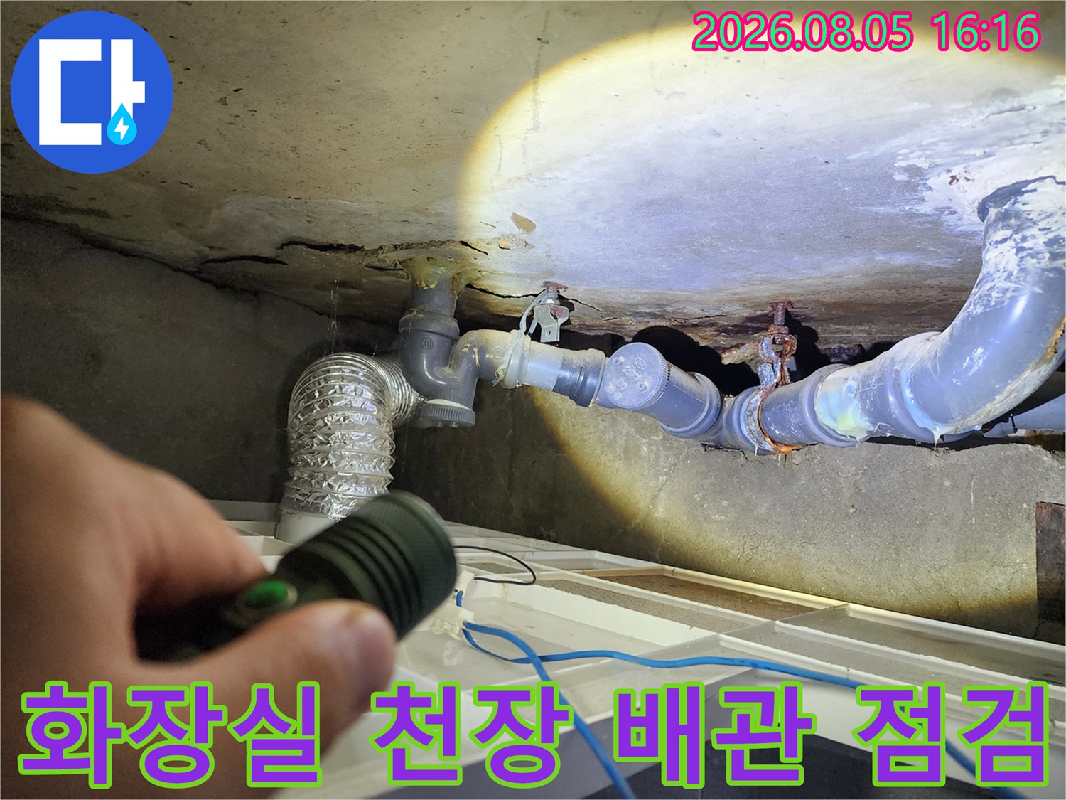 손전등으로 비춰본 화장실 천장 내부의 노후된 배관 연결부