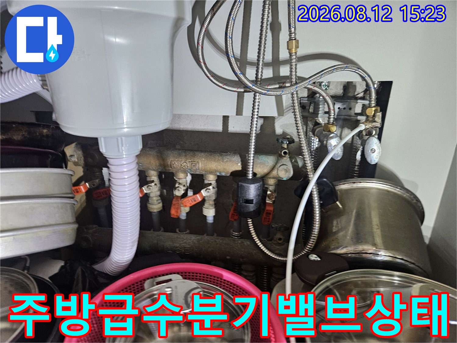 다양한 굵기의 수도 배관과 빨간색 손잡이 밸브들이 설치된 싱크대 하부 사진