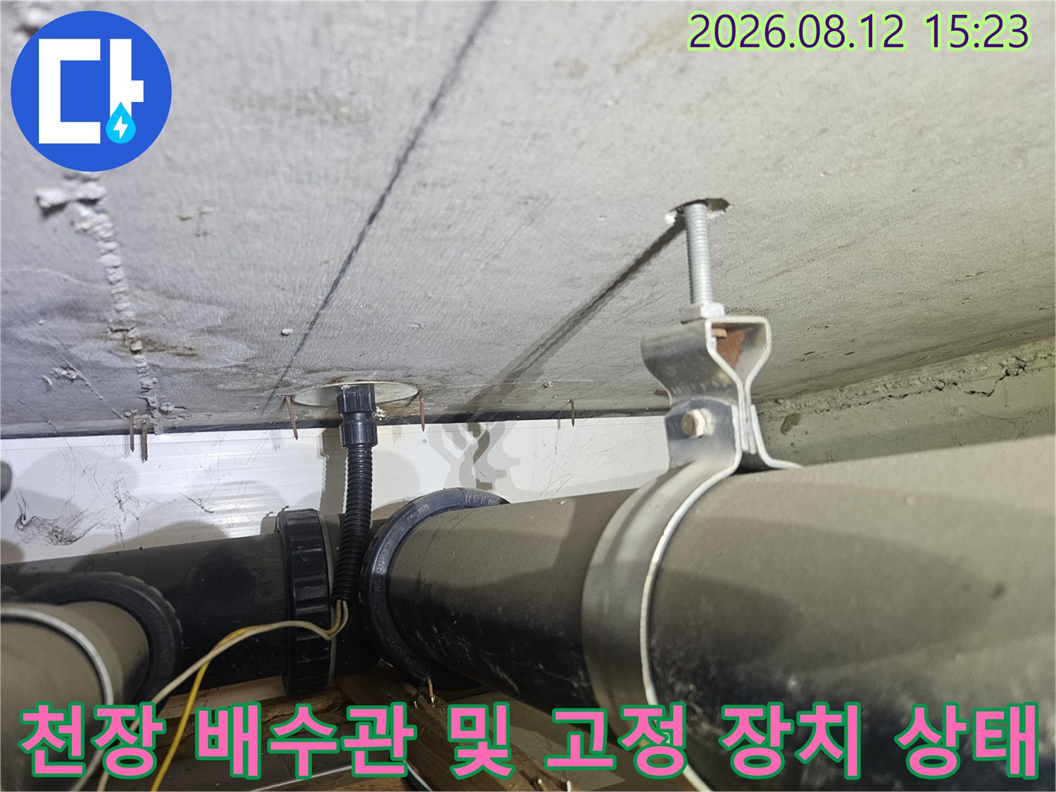 콘크리트 천장에 설치된 검은색 배수 배관과 금속제 고정 브라켓-전선관 연결 부위