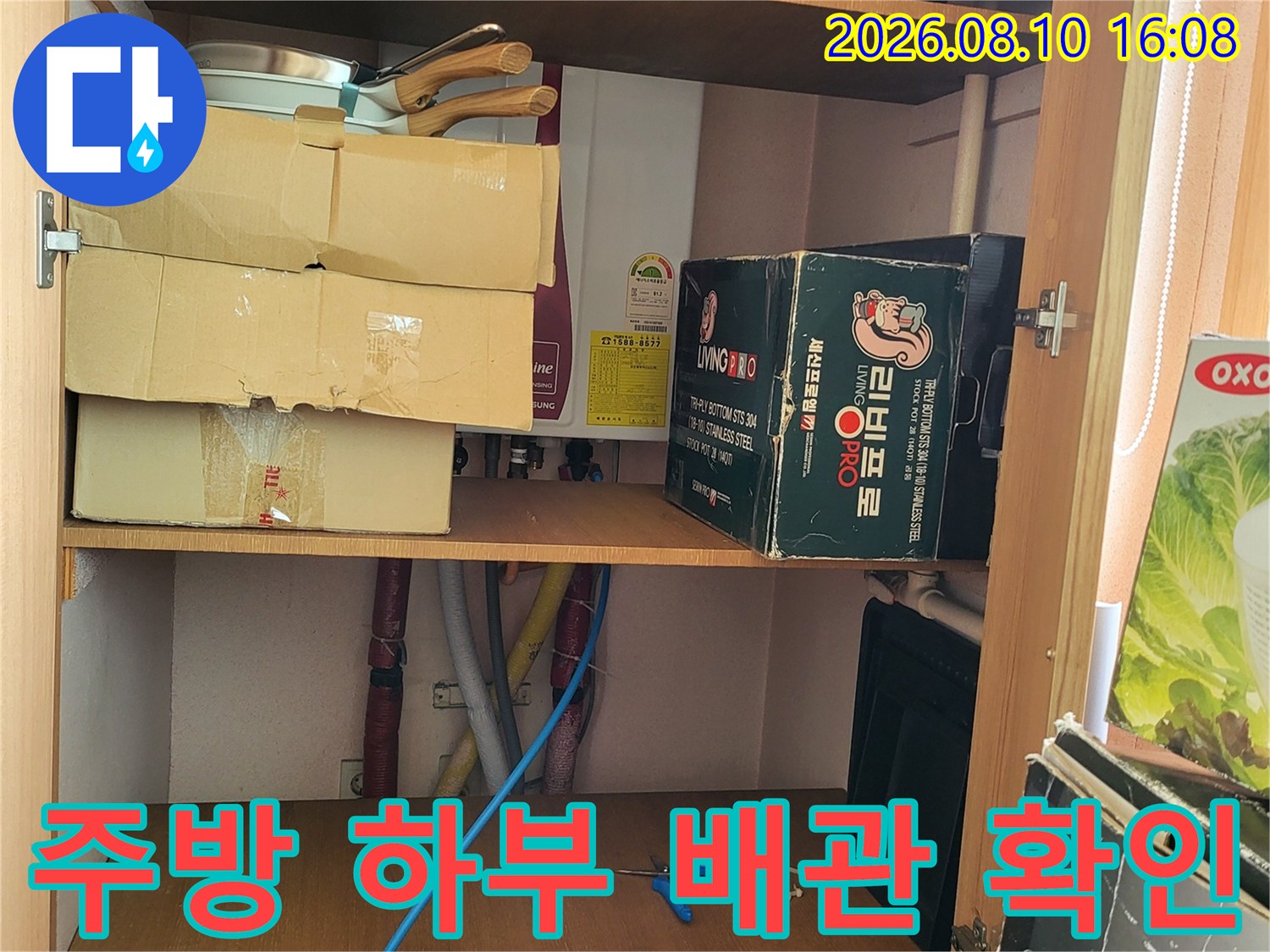 싱크대 아래 수납칸의 물건들과 연결된 배관 상태를 점검하고 있습니다.