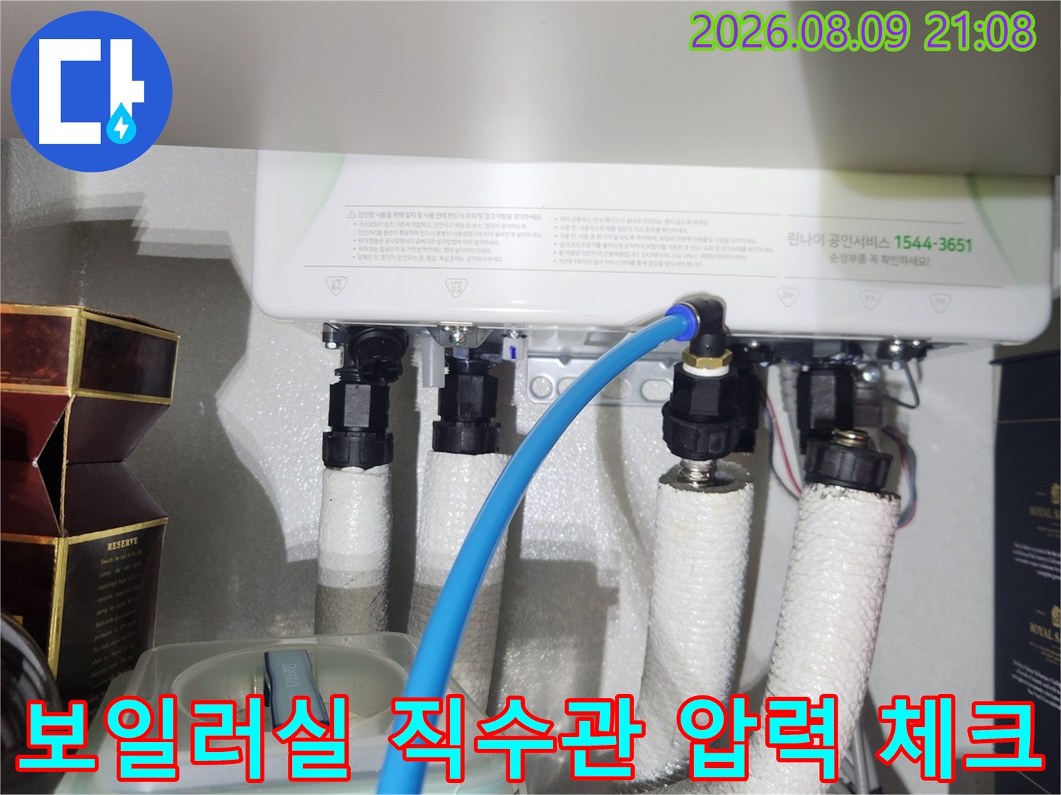 흰색 보온재로 덮인 보일러 하부 배관에 파란색 호스가 연결된 모습