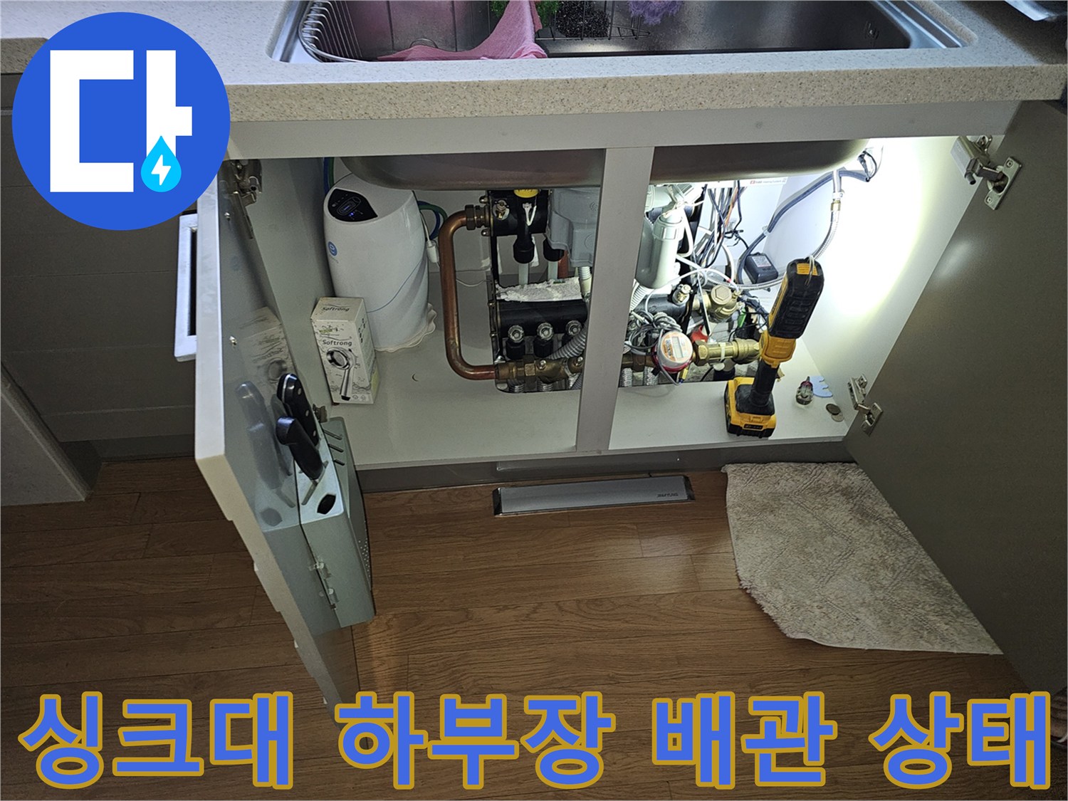 싱크대 아래쪽 수도 배관과 전동 드릴 등 작업 도구가 놓여 있는 점검 현장