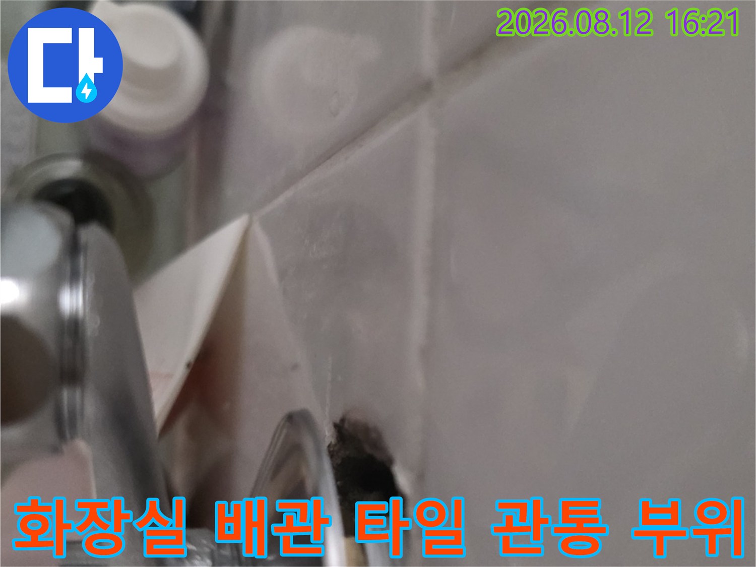 금속제 세면대 배관이 흰색 타일을 관통하여 설치된 연결 지점-누수 발생 구간