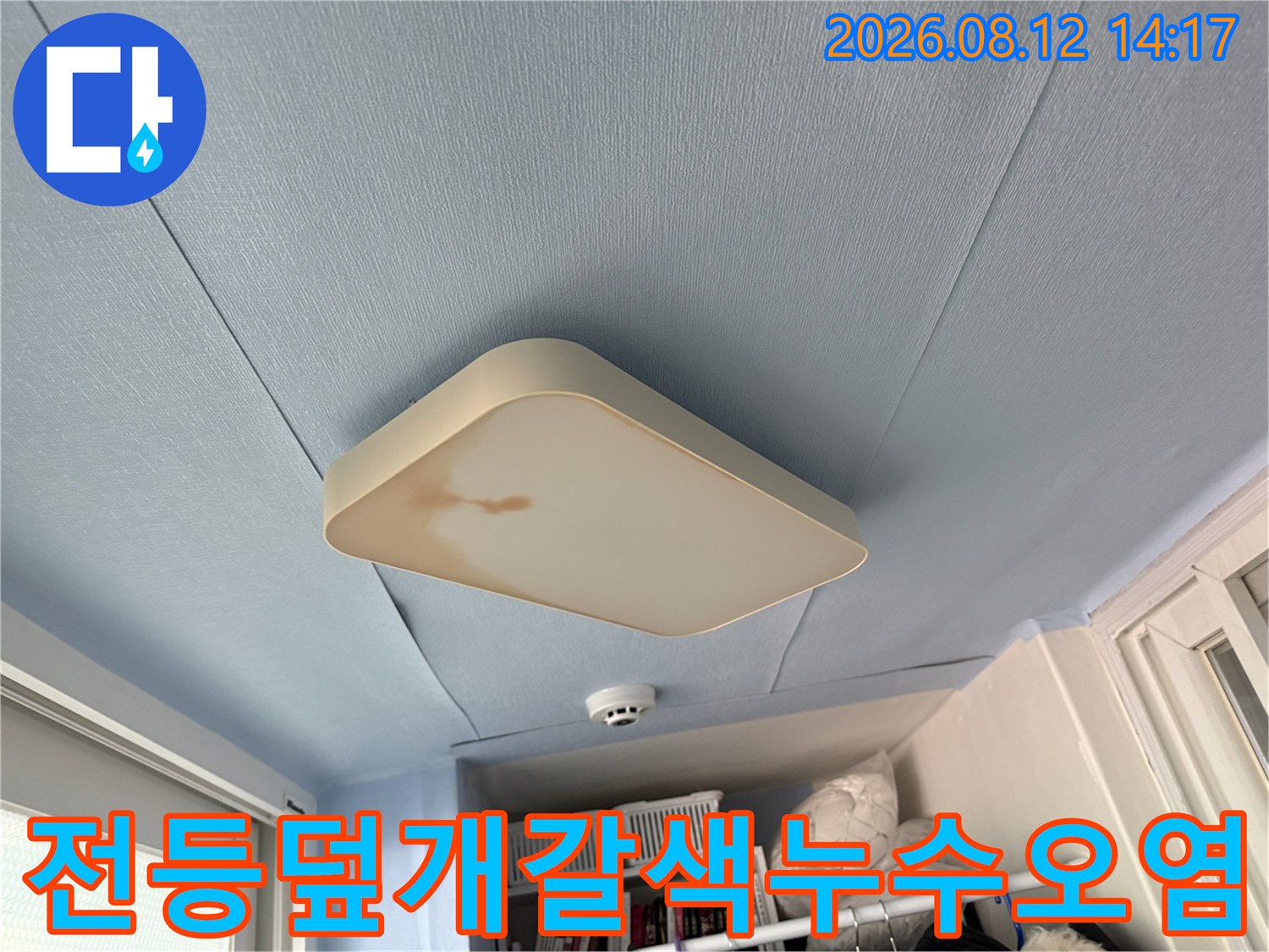 하늘색 천장의 사각형 조명 덮개 가장자리에 갈색의 물 얼룩이 형성된 사진