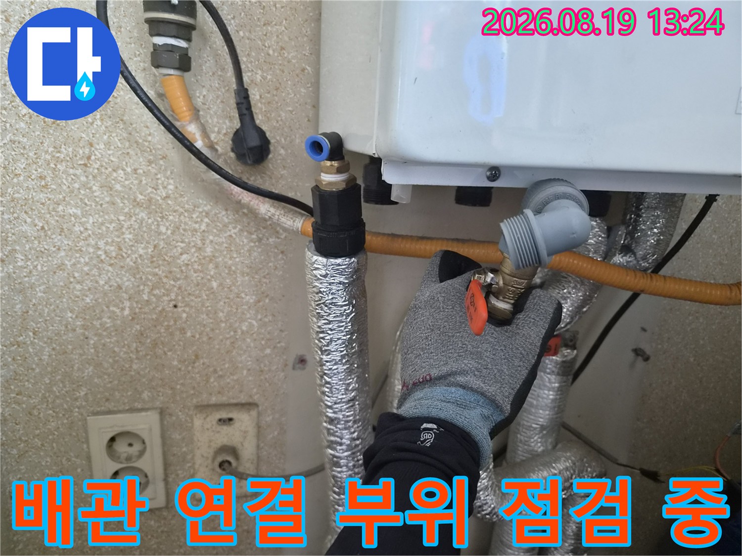 작업자가 보일러 하단 배관의 밸브와 연결부를 면밀히 살피고 있습니다.