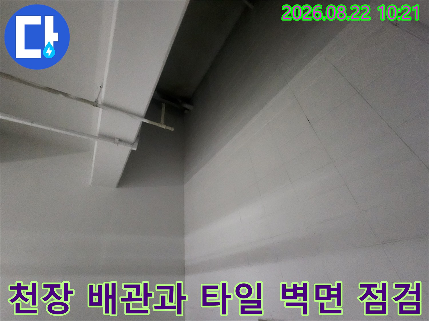 지하주차장 천장에 설치된 배관과 흰색 타일 벽면의 근접 촬영