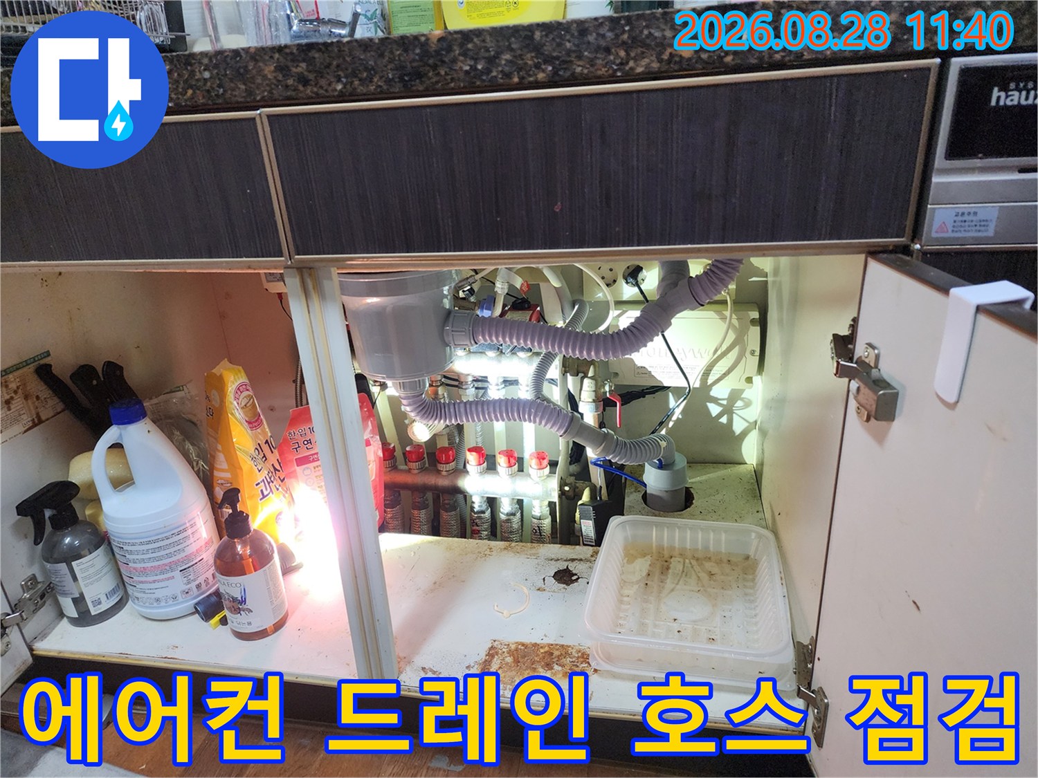 싱크대 하부장 안쪽 에어컨 배수 호스와 여러 연결 배관들의 배치 상태