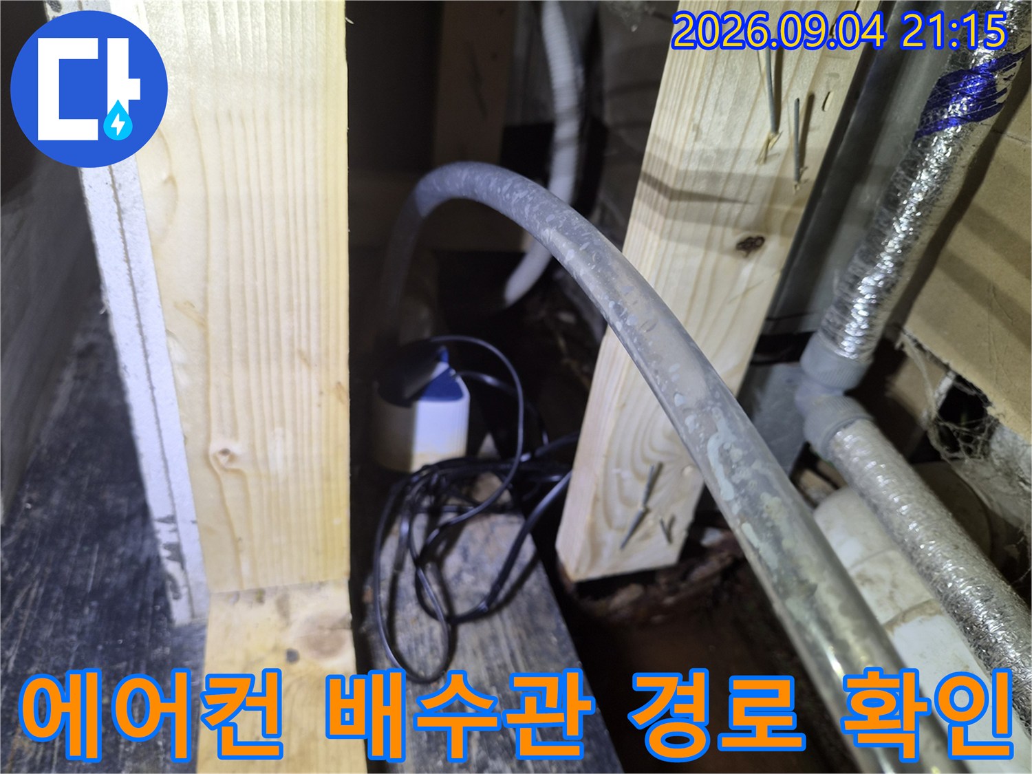 천장 내부 목재 프레임 사이로 연결된 에어컨 드레인 호스 및 배관 모습