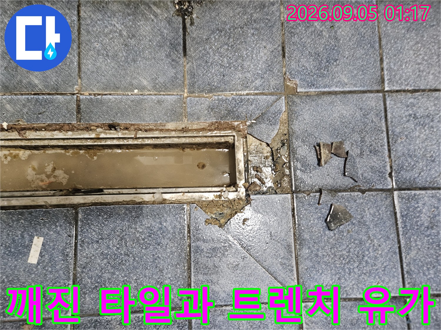 유가 주변의 깨진 타일 조각과 노출된 배수구 구조물