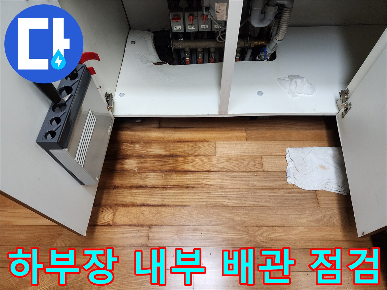 싱크대 하부장 내부에 노출된 급수 및 배수 배관의 모습입니다.