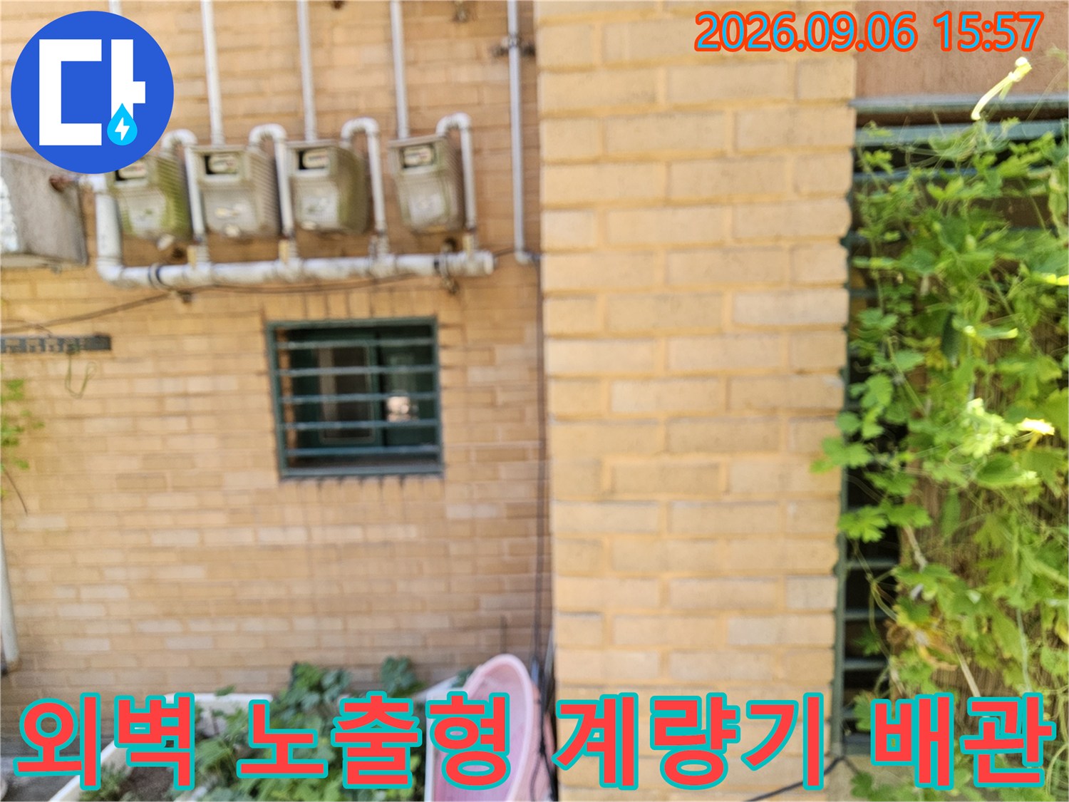 건물 벽돌 외벽에 설치된 수도 계량기와 연결된 배관입니다.