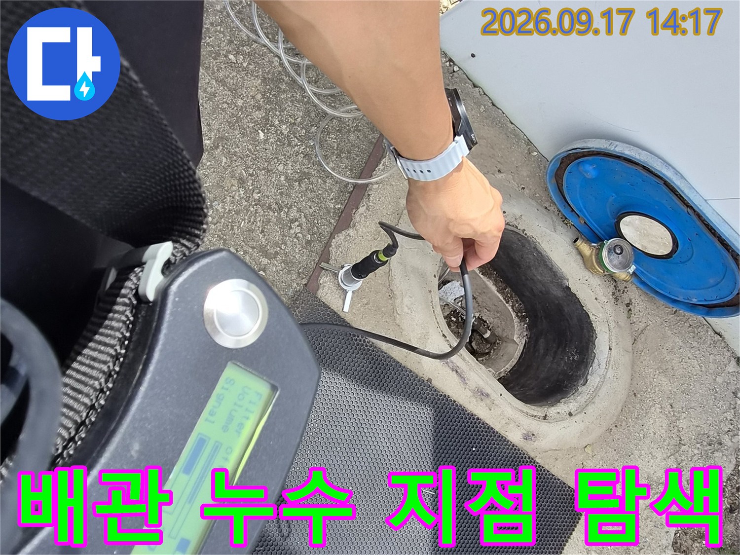땅속에 매립된 배관의 누수를 확인하기 위해 청음식 장비를 배관 근처에 대고 있는 장면입니다.